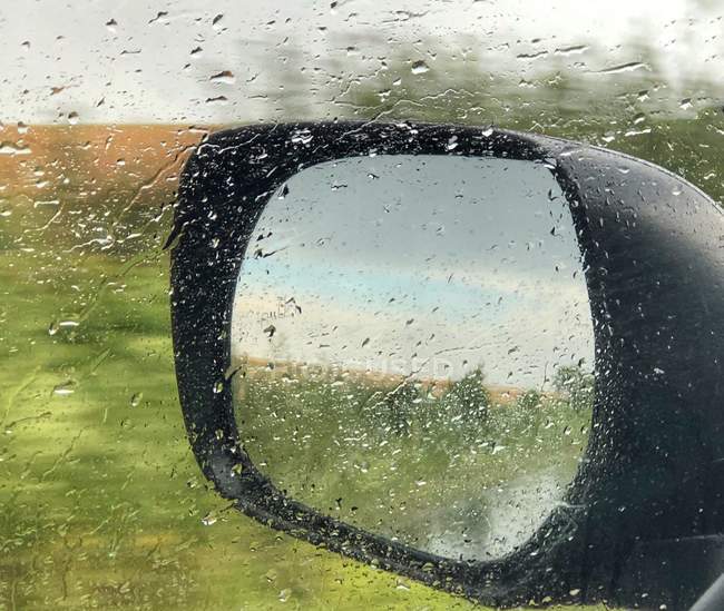Крупним планом дзеркало крила через вікно мокрого автомобіля — стокове фото