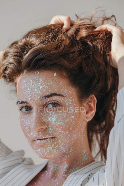 Portrait of a beautiful woman covered in glitter with her hands in her hair — Stock Photo