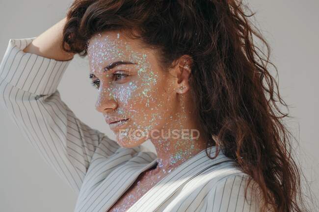 Portrait of a beautiful woman covered in glitter with her hands in her hair — Stock Photo