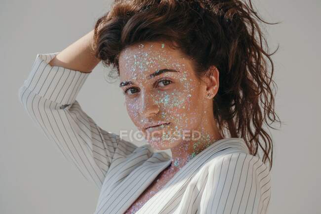 Retrato de una hermosa mujer cubierta de brillo con las manos en el pelo - foto de stock
