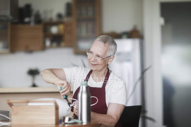 Frau sitzt an einem Tisch und repariert eine Lampe — Stockfoto