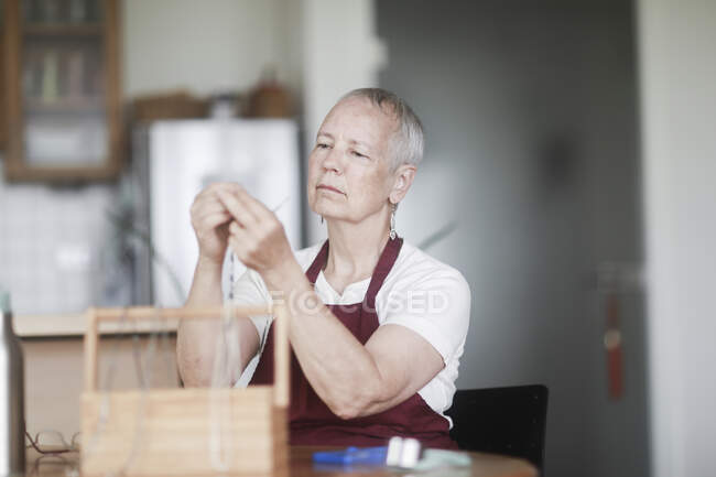 Woman sitting at a table fixing a necklace — Stock Photo