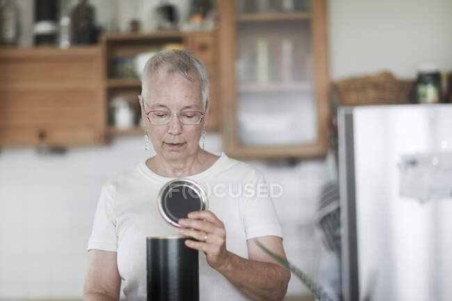 Mujer de pie en la cocina mirando una lata - foto de stock