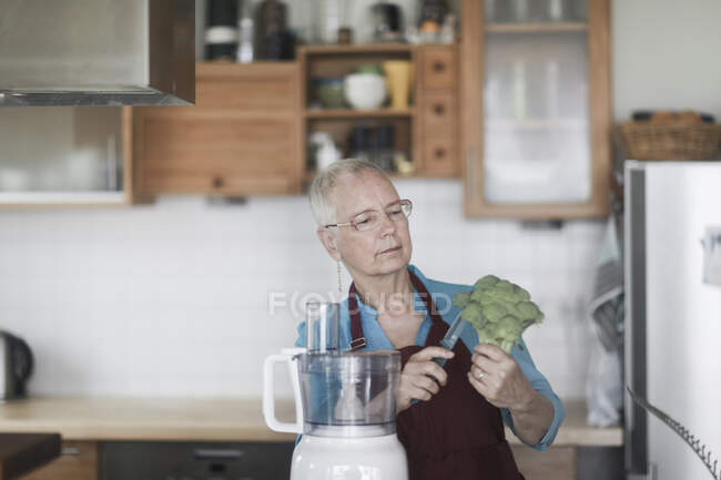 Woman standing in the kitchen preparing broccoli — Stock Photo