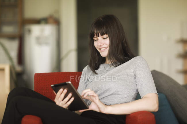 Mulher sentada em uma poltrona usando um tablet digital — Fotografia de Stock