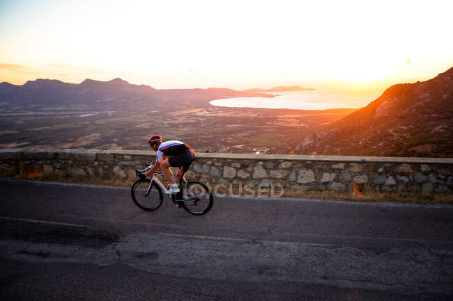Mann radelt bei Sonnenuntergang auf Bergstraße, Korsika, Frankreich — Stockfoto