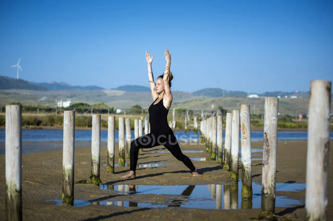 Woman standing on Los Lances beach dong a high lunge yoga pose, Tarifa, Cádiz, Andaluzia, Espanha — Fotografia de Stock