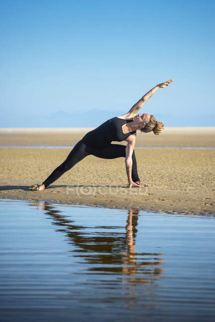 Woman on Los Lances beach doing an extended side angle yoga pose, Tarifa, Cádiz, Andaluzia, Espanha — Fotografia de Stock