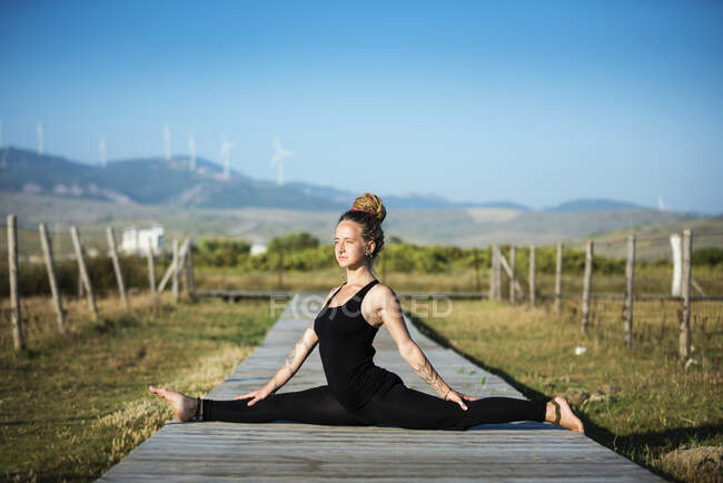 Femme sur la plage de Los Lances faisant face splits pose de yoga, Le parc naturel du détroit, Tarifa, Cadix, Andalousie, Espagne — Photo de stock