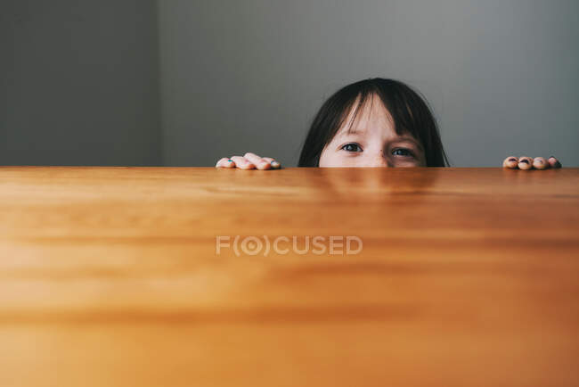 Chica escondida detrás de una mesa - foto de stock