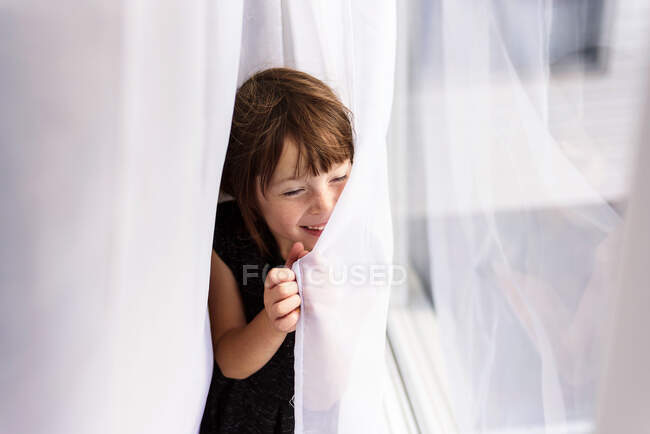 Souriante fille se cachant derrière un rideau — Photo de stock
