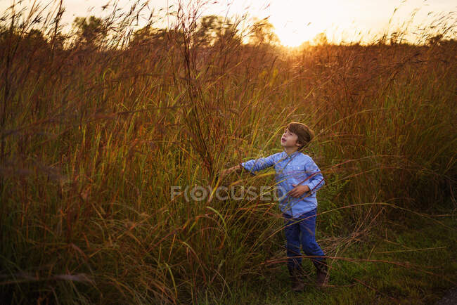 Junge spielt im langen Gras bei Sonnenuntergang, Vereinigte Staaten — Stockfoto