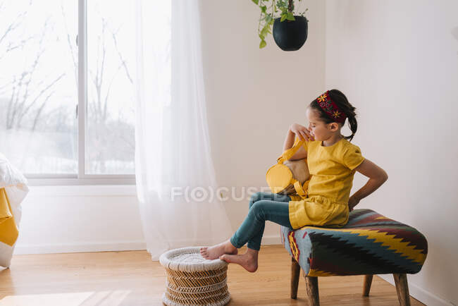 Girl sitting on a stool putting on her backpack — Stock Photo