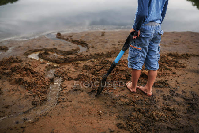 Menino de pé em uma praia segurando uma pá — Fotografia de Stock
