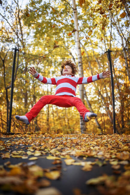 Niño saltando en un trampolín cubierto de hojas de otoño, Estados Unidos - foto de stock