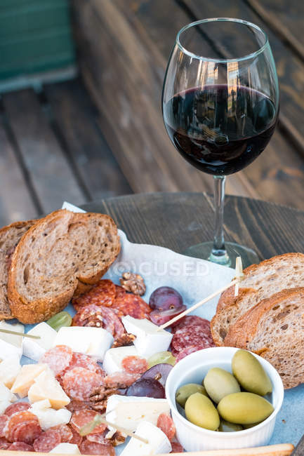 Close-up de queijo, charcutaria, azeitonas, uvas e pão em uma mesa com um copo de vinho tinto — Fotografia de Stock