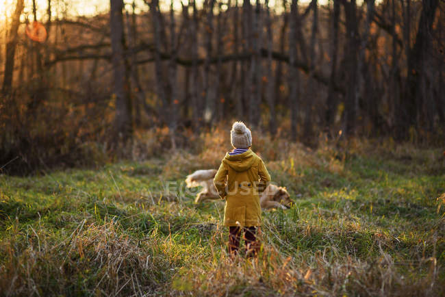 Fille debout dans les bois regardant son chien courir partout, États-Unis — Photo de stock