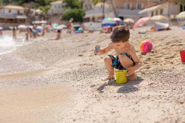 Menino enchendo um balde com areia na praia, Grécia — Fotografia de Stock