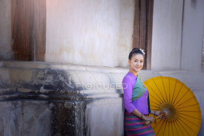 Porträt einer Frau in traditioneller thailändischer Kleidung, die sich an ein Gebäude lehnt, Thailand — Stockfoto