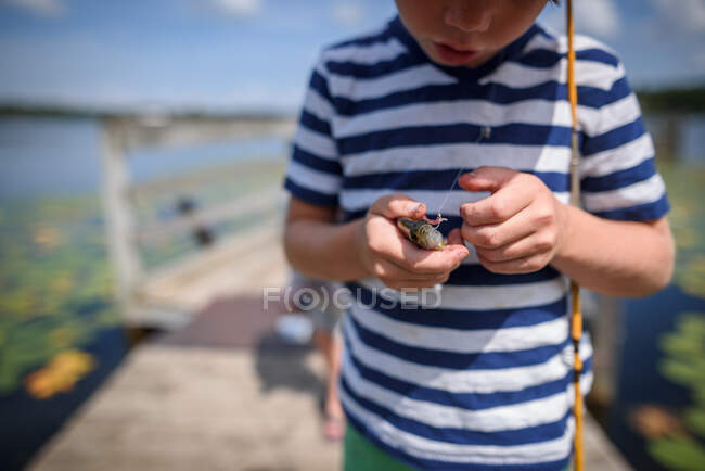Garçon debout sur un quai tenant une prise fraîche de poisson, États-Unis — Photo de stock