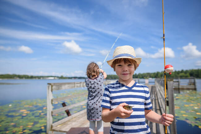 Двое детей ловят рыбу на причале летом, США — стоковое фото