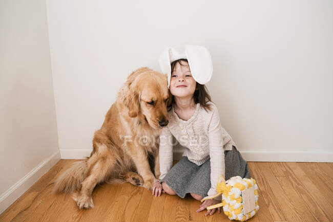 Retrato de uma menina sorrindo usando orelhas de coelho sentado no chão com seu cão — Fotografia de Stock