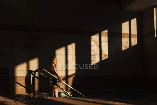 Хлопчик стоїть на сходах у басейні в тіні — стокове фото