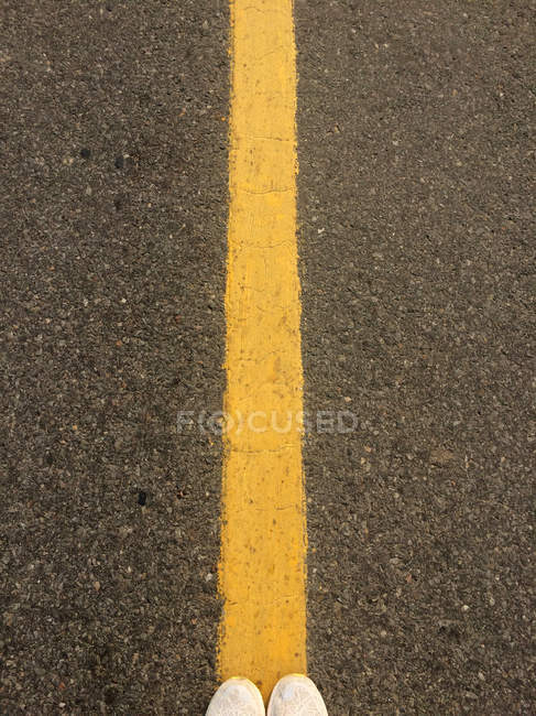 Woman feet standing on a yellow line in the road — Stock Photo