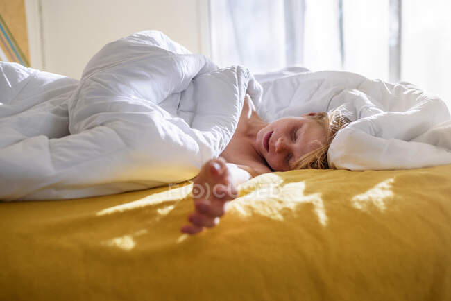 Boy lying in bed sleeping in morning light — Stock Photo