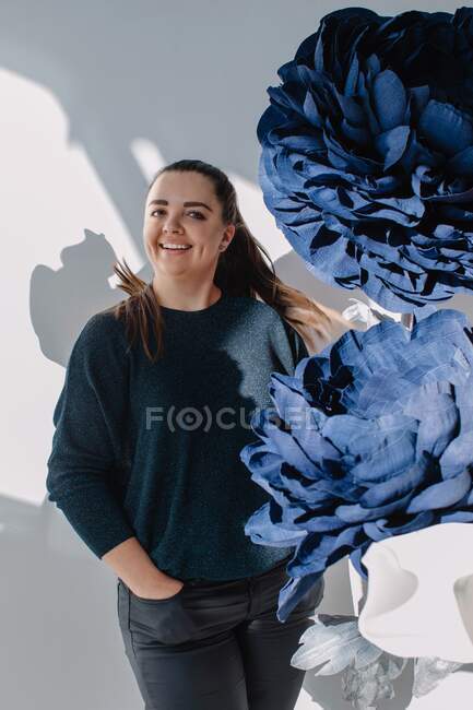 Portrait of a smiling woman standing next to giant artificial flowers — Stock Photo