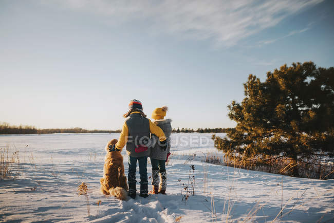 Niño y niña con su perro en un campo cubierto de nieve, Estados Unidos - foto de stock