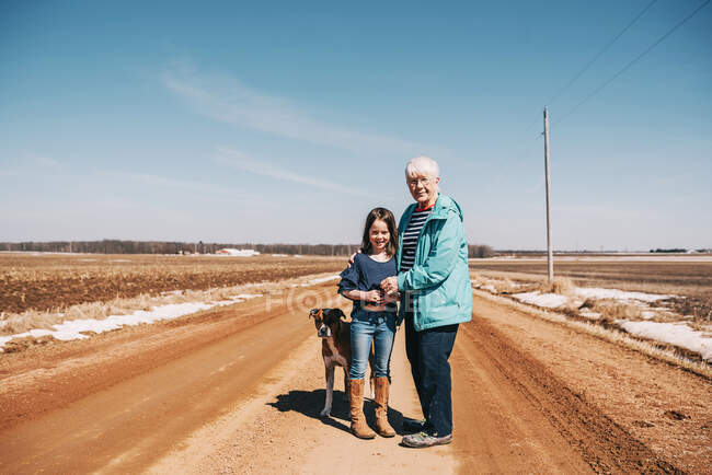 Grandmother and granddaughter standing on a road with their dog, United States — Stock Photo
