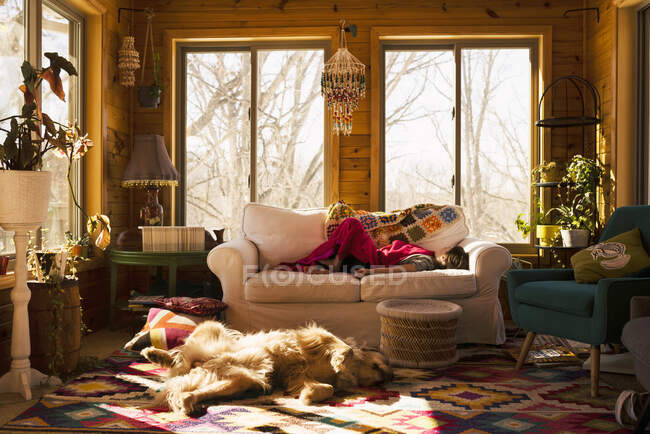 Menina dormindo em um sofá com seu cão no chão ao lado dela — Fotografia de Stock