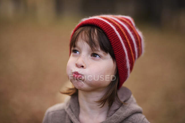 Retrato de uma menina com um chapéu de lã puxando caras engraçadas — Fotografia de Stock