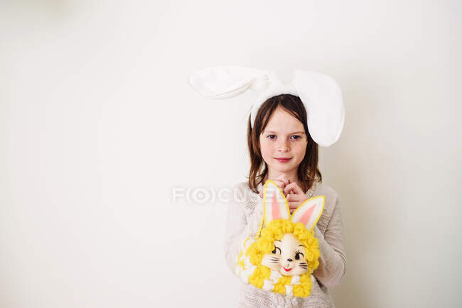 Retrato de una chica sonriente con orejas de conejo sosteniendo una bolsa de conejo - foto de stock