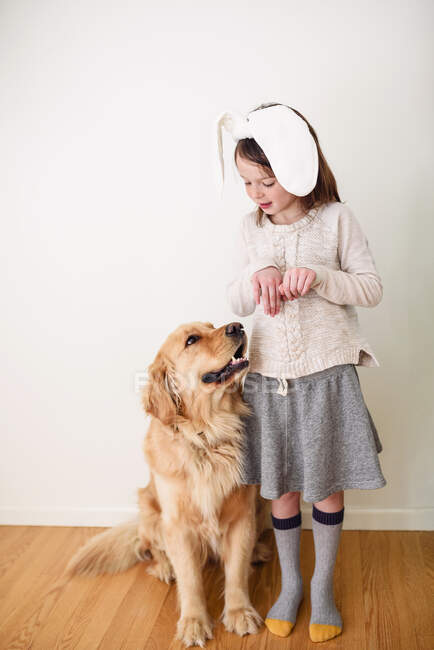 Retrato de una chica sonriente con orejas de conejo de pie junto a su perro - foto de stock