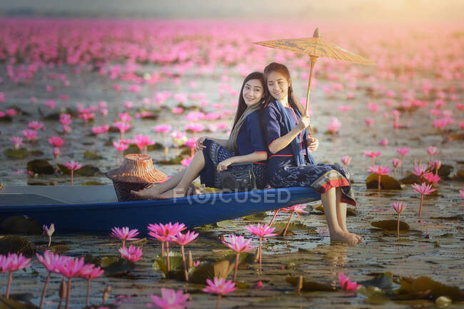 Dos mujeres sentadas en un barco en un lago de flores de loto, Tailandia - foto de stock