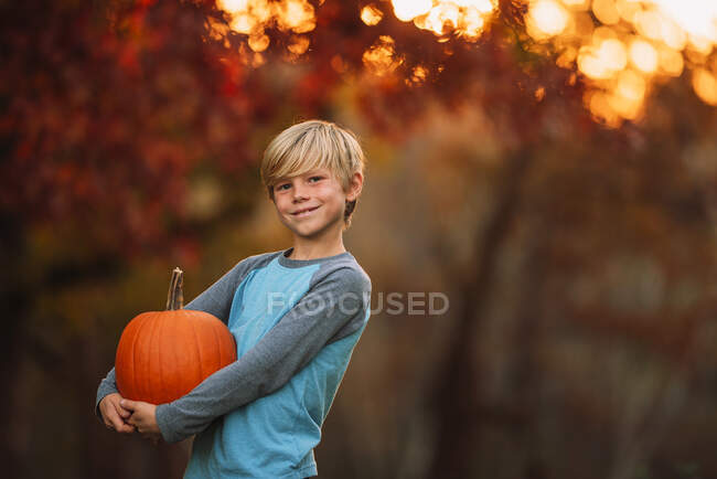 Retrato de un niño de pie en un jardín con una calabaza, Estados Unidos - foto de stock