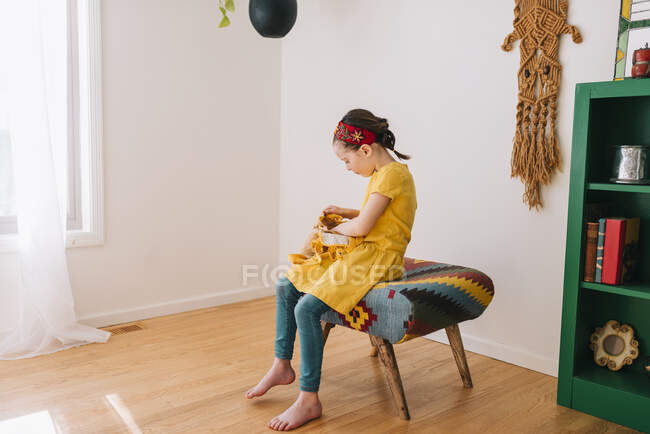 Girl sitting on a stool looking in her backpack — Stock Photo