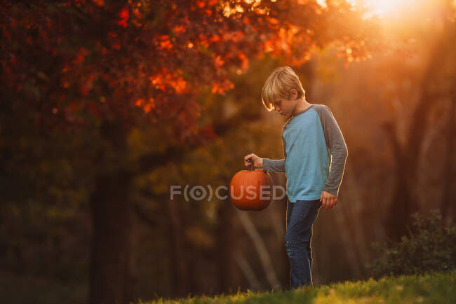 Menino de pé em um jardim com uma abóbora, Estados Unidos — Fotografia de Stock