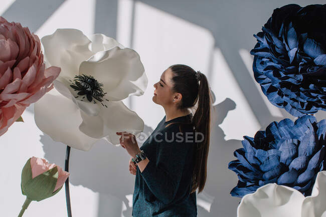 Retrato de uma mulher de pé ao lado de flores artificiais gigantes — Fotografia de Stock
