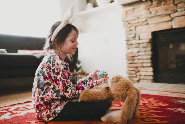 Girl wearing bunny ears playing with a soft toy rabbit — Stock Photo