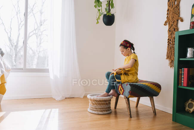 Girl sitting on a stool opening her backpack — Stock Photo