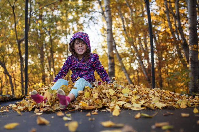 Улыбающаяся девушка, сидящая на стоге осенних листьев на батуте, США — стоковое фото