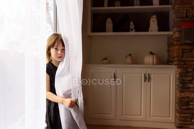 Sonriente chica escondida detrás de una cortina - foto de stock
