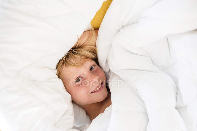 Vista aérea de un niño sonriente acostado en la cama - foto de stock