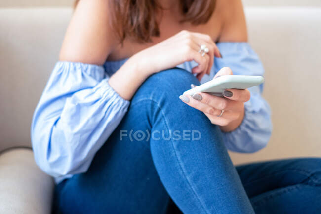Mulher sentada no sofá usando um telefone celular — Fotografia de Stock