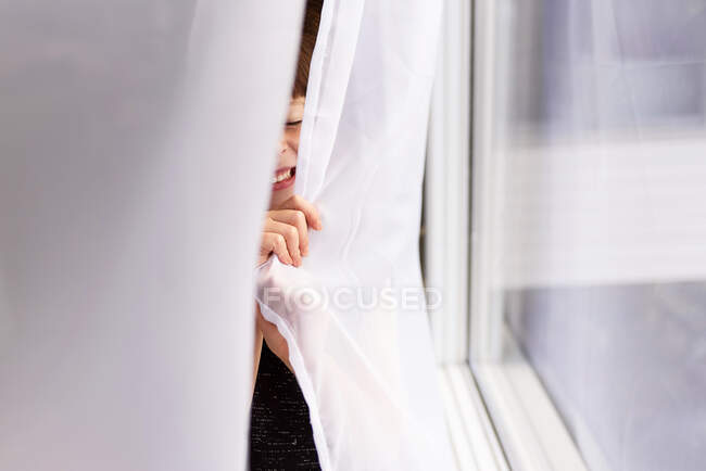 Fille se cachant derrière un rideau riant — Photo de stock