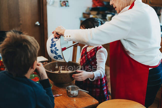 Two children helping their grandmother bake a cake — Stock Photo