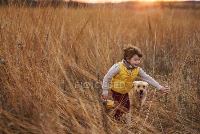 Boy and his dog running through a field at sunset, United States — Stock Photo